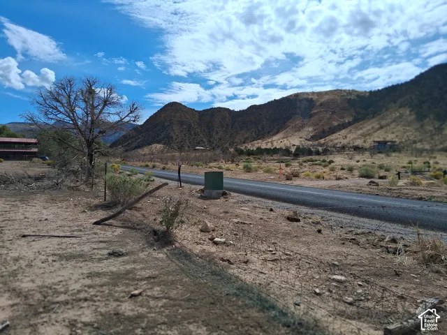 Expansive vacant land featuring a paved road, natural desert landscape, and prominent mountain backdrops