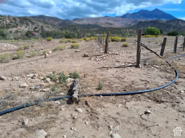 Expansive terrain featuring natural arid vegetation, post-and-wire perimeter fencing, mountain backdrop, and installed irrigation line