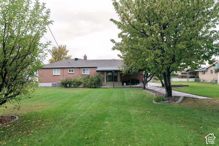 Brick exterior siding, asphalt shingle roof, paved concrete walkway, and mature trees situated on a grass lawn