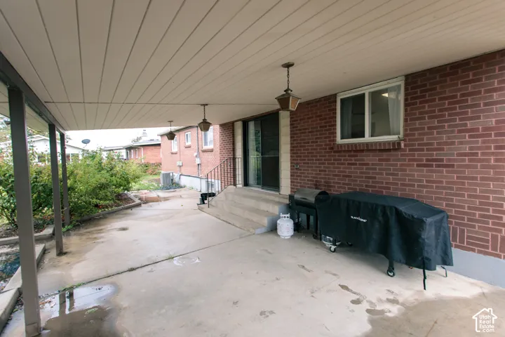 Covered concrete patio featuring a red brick exterior, overhead pendant lighting, sliding glass door, and masonry steps with metal railing