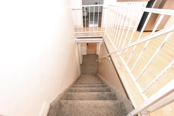 Staircase featuring neutral carpeting, a metal handrail, and a white metal safety railing