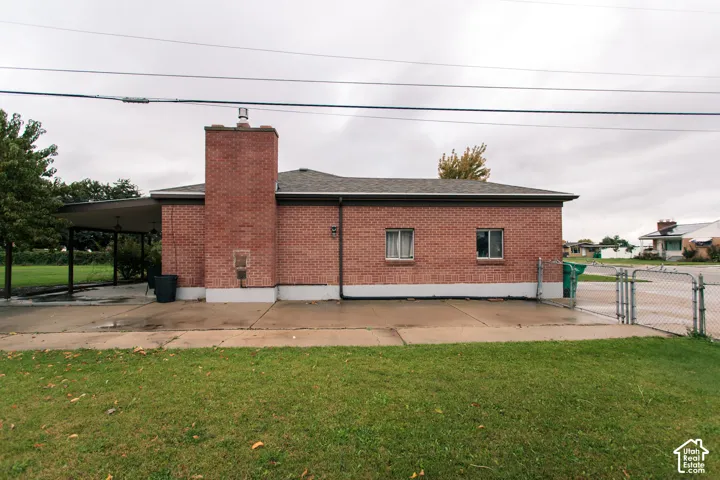 Exterior featuring red brick masonry, a brick chimney, a concrete patio, a covered carport, and perimeter chain-link fencing