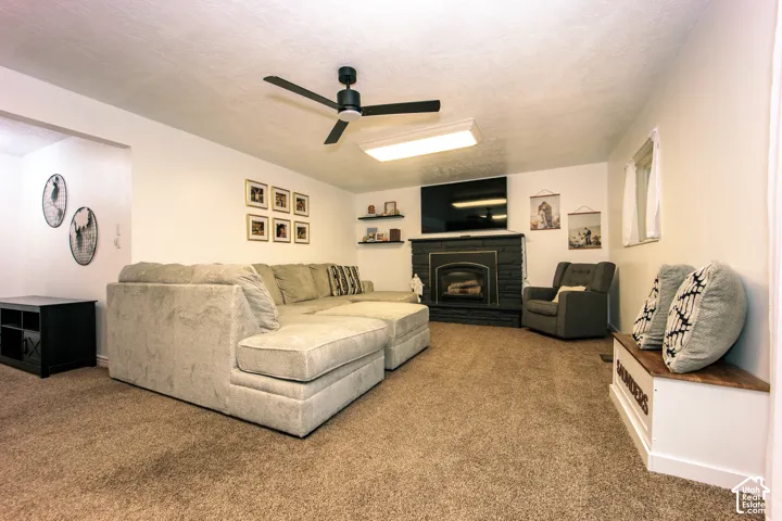 Living area featuring a floor-to-ceiling painted brick fireplace, wall-mounted shelving, neutral carpeting, and a ceiling fan