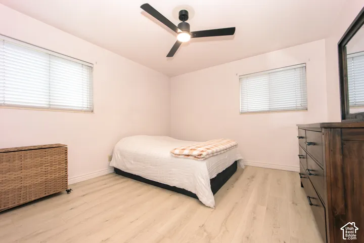 Neutral-toned room featuring wood-finish flooring, dual windows with horizontal blinds, and a matte black three-blade ceiling fan with integrated lighting