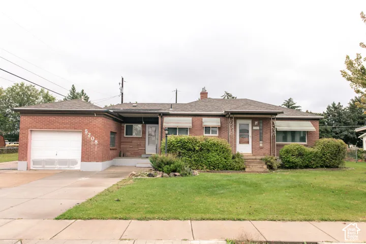 Single-story brick exterior featuring a hip roof, attached garage, concrete driveway, and front-facing awning windows