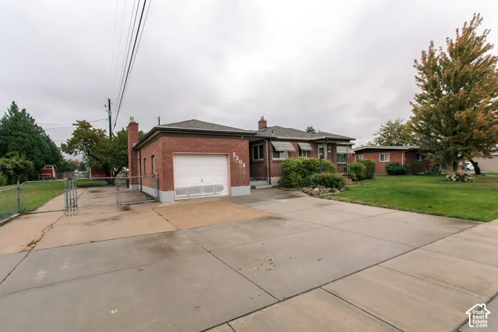 Brick exterior featuring an attached single-car garage, concrete driveway, and chain-link fenced side parking area