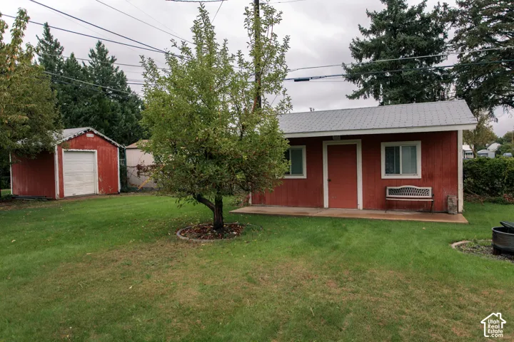 Backyard featuring an expansive lawn, two detached structures with metal roofing, a concrete patio, and mature trees