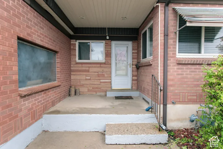 Covered entry porch featuring brick masonry, horizontal stone veneer, concrete steps, and a metal handrail