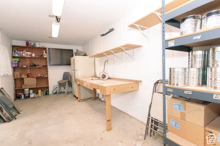 Utility space featuring concrete flooring, built-in wooden workbench, wall-mounted cabinetry, integrated wall shelving, and fluorescent overhead lighting