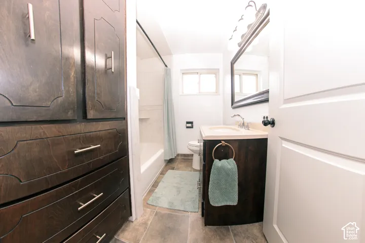 Bathroom featuring dark-stained wood cabinetry, stone-finish flooring, a vanity with a neutral solid surface countertop, and a shower-tub combination with tiled surround