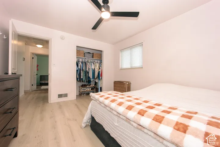 Wood-finish flooring, ceiling fan with integrated lighting, and a reach-in closet featuring built-in shelving