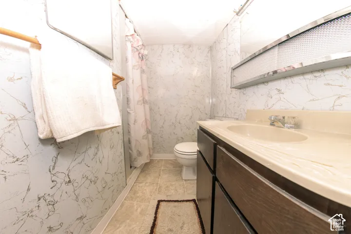 Bathroom featuring a vanity with dark wood-finish cabinetry, an integrated sink with a neutral countertop, textured wall coverings, and tile flooring