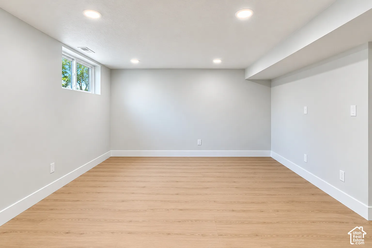 Neutral-toned interior space featuring wood-finish flooring, recessed lighting, and a single window