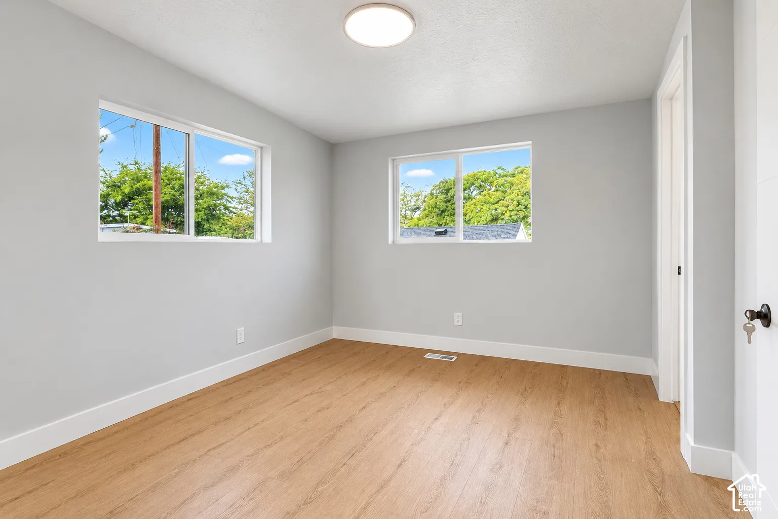 Neutral interior room featuring wood-finish flooring, two sliding windows, and a flush-mount ceiling light fixture