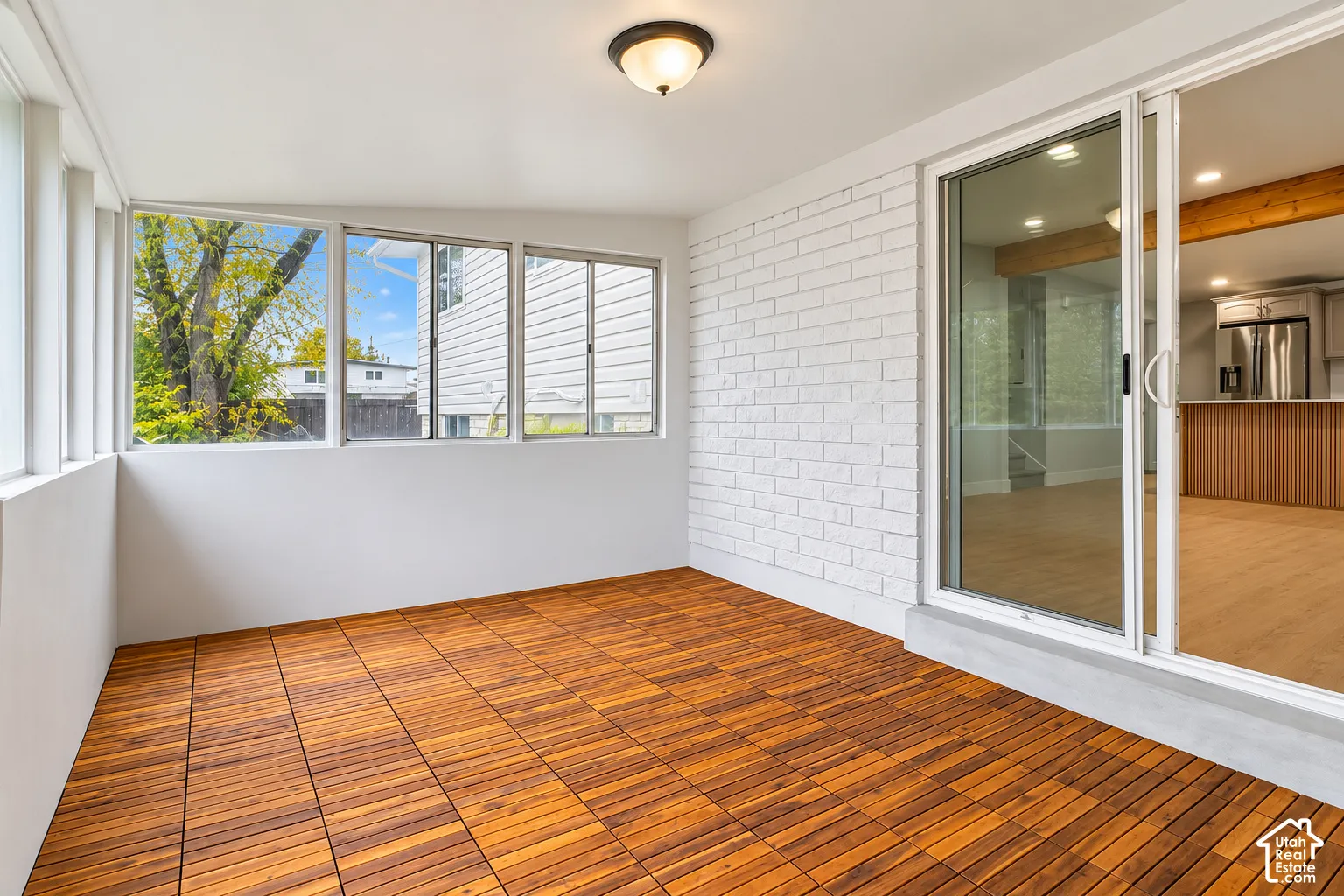 Enclosed sunroom featuring wood-finish flooring, white-painted brick wall, multi-pane window configuration, and sliding glass entry door