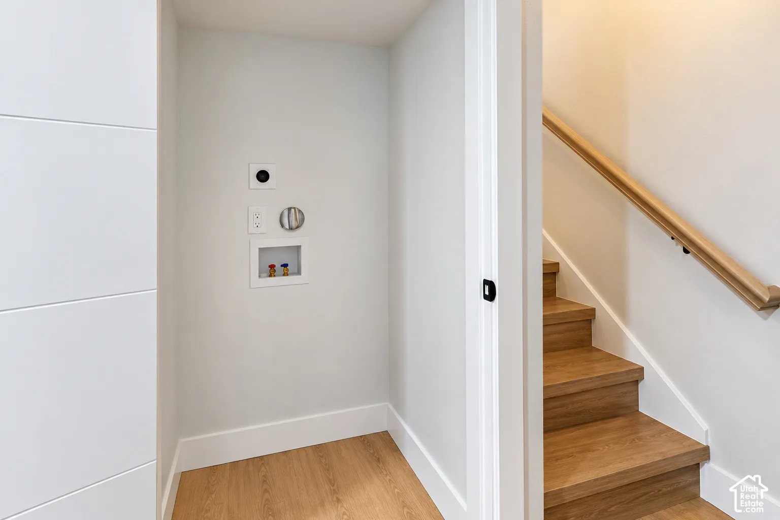 Dedicated laundry hookup area with wood-finish flooring and wood-finish staircase featuring a matching handrail