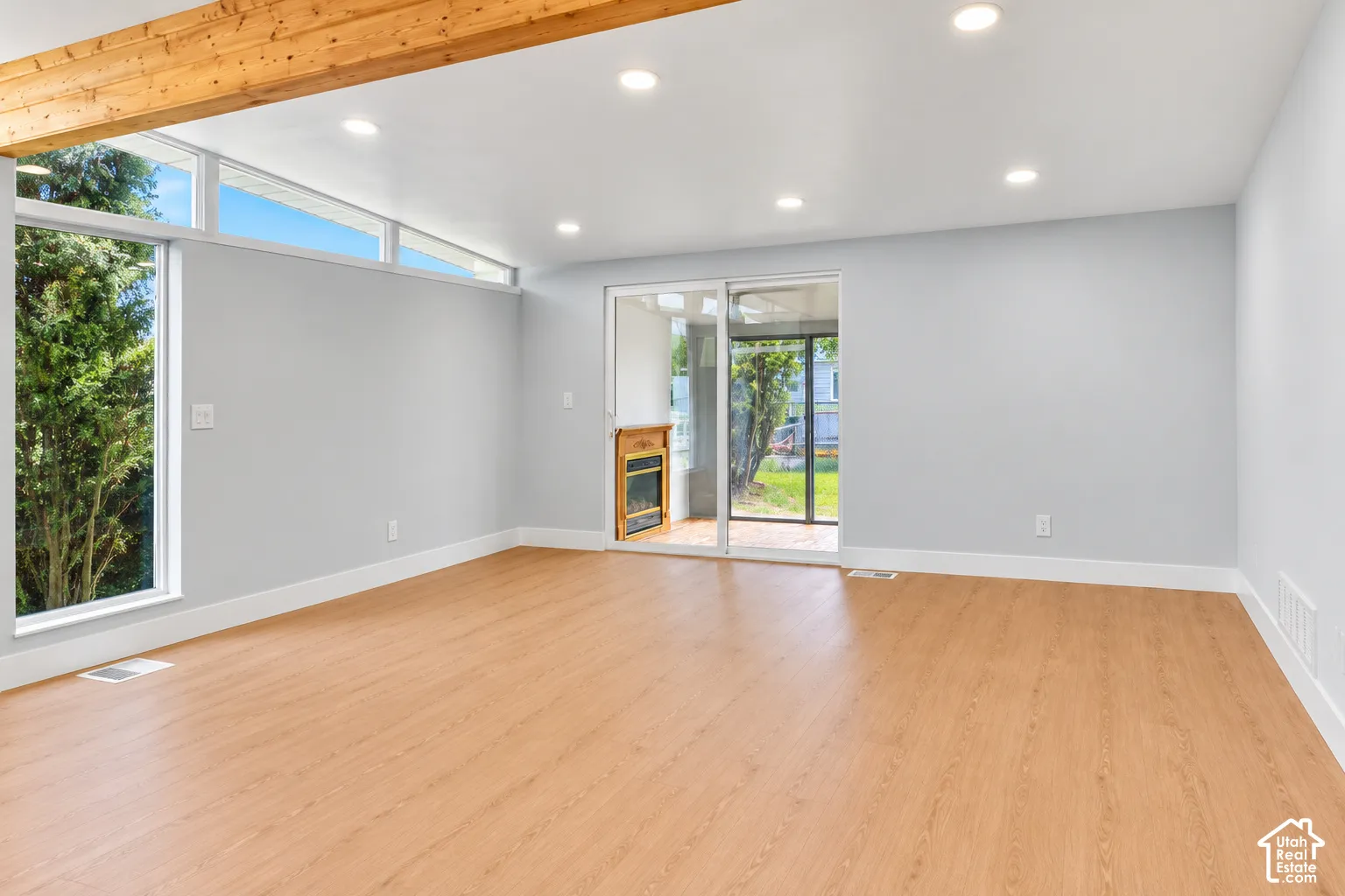 Interior space featuring wood-finish flooring, recessed lighting, clerestory windows, a prominent exposed wood beam, and a sliding glass door