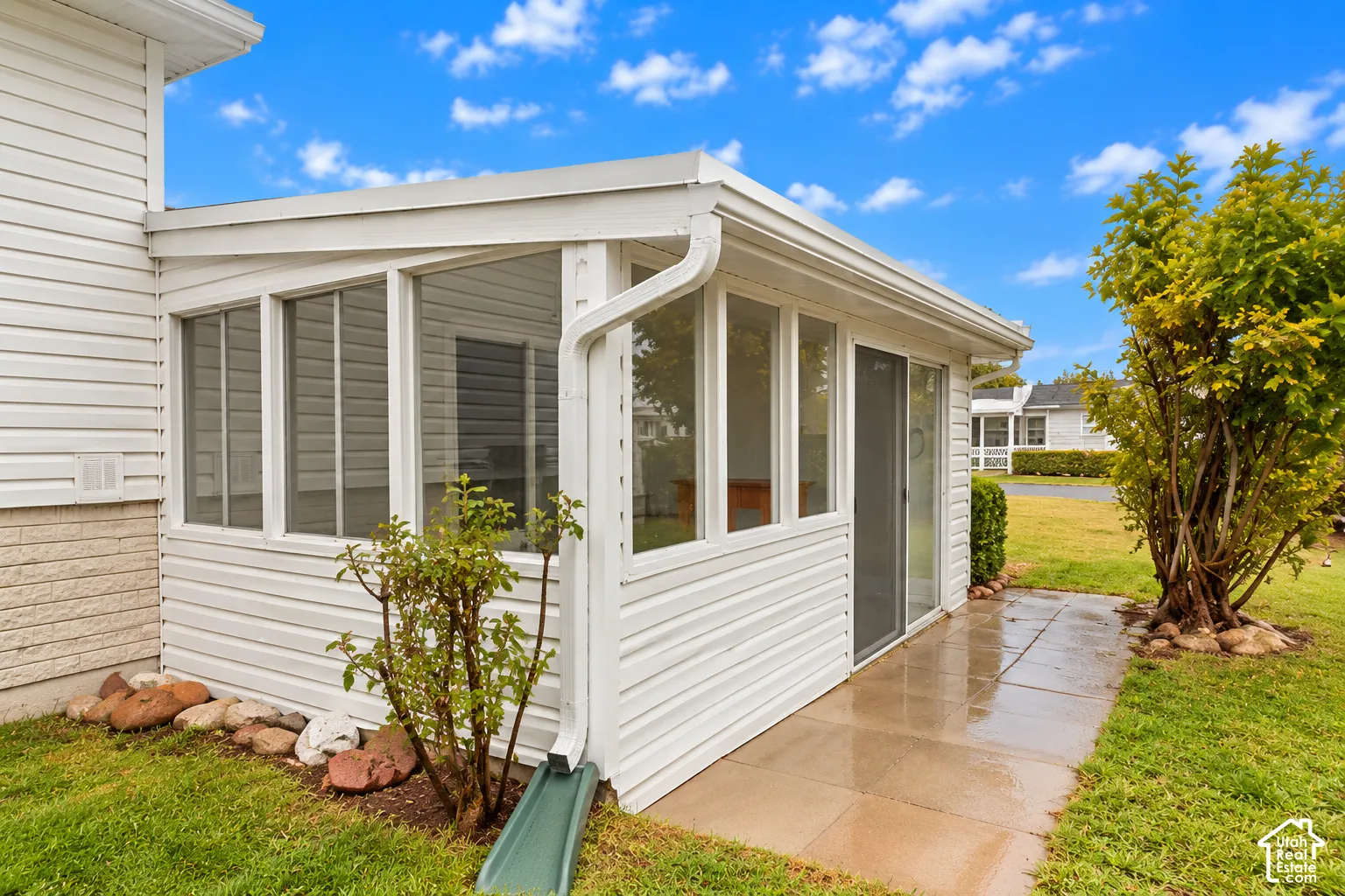 Enclosed sunroom featuring white siding, multiple glass window panes, a screen door, and an attached concrete patio