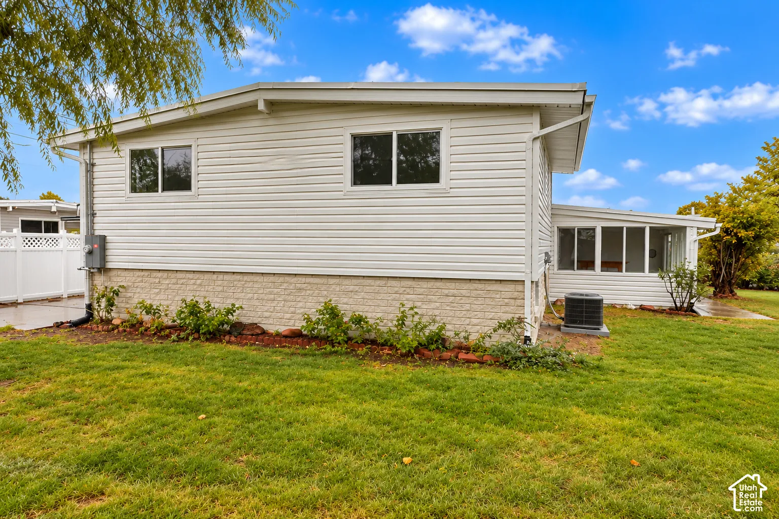 Exterior featuring light-colored horizontal siding, stone-textured masonry foundation, rear screened-in patio, and vinyl perimeter fencing