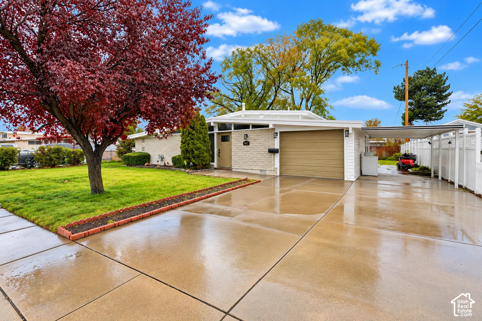 Single-story exterior featuring light-toned masonry, a horizontal-panel garage door, a covered side carport, and a manicured front lawn