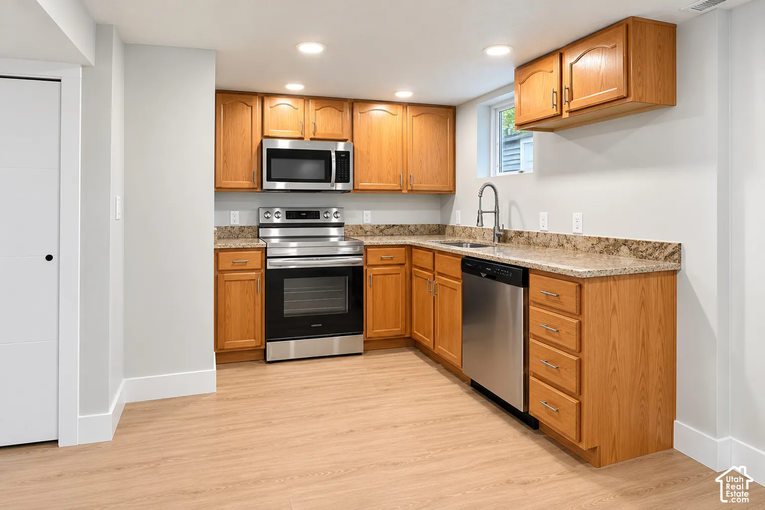 Kitchen featuring wood cabinetry, stainless steel appliances, speckled stone-finish countertops, recessed lighting, and wood-finish flooring