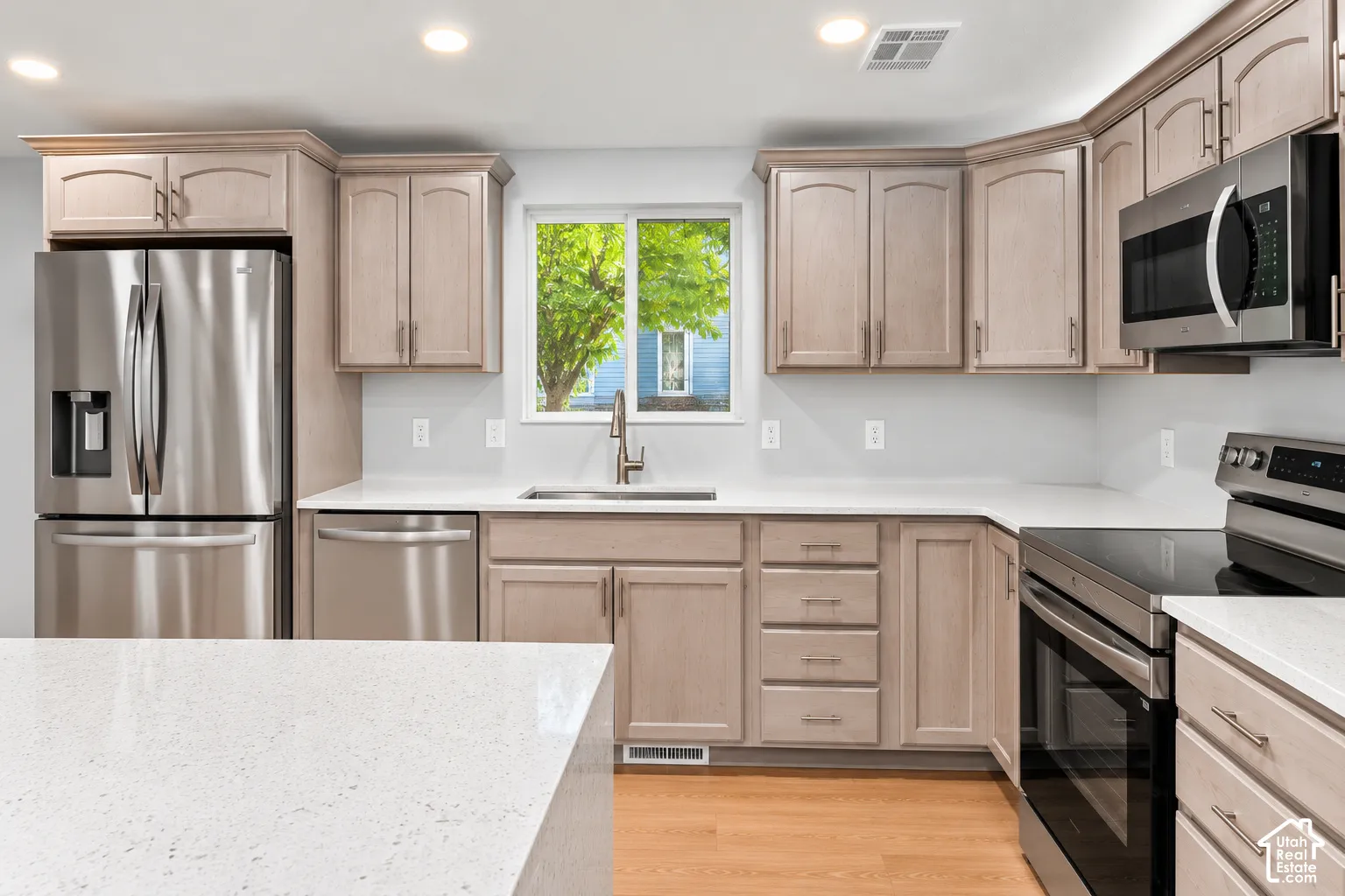Kitchen featuring light-finish cabinetry, white countertops, stainless steel appliances, a recessed sink with a gooseneck faucet, and wood-finish flooring
