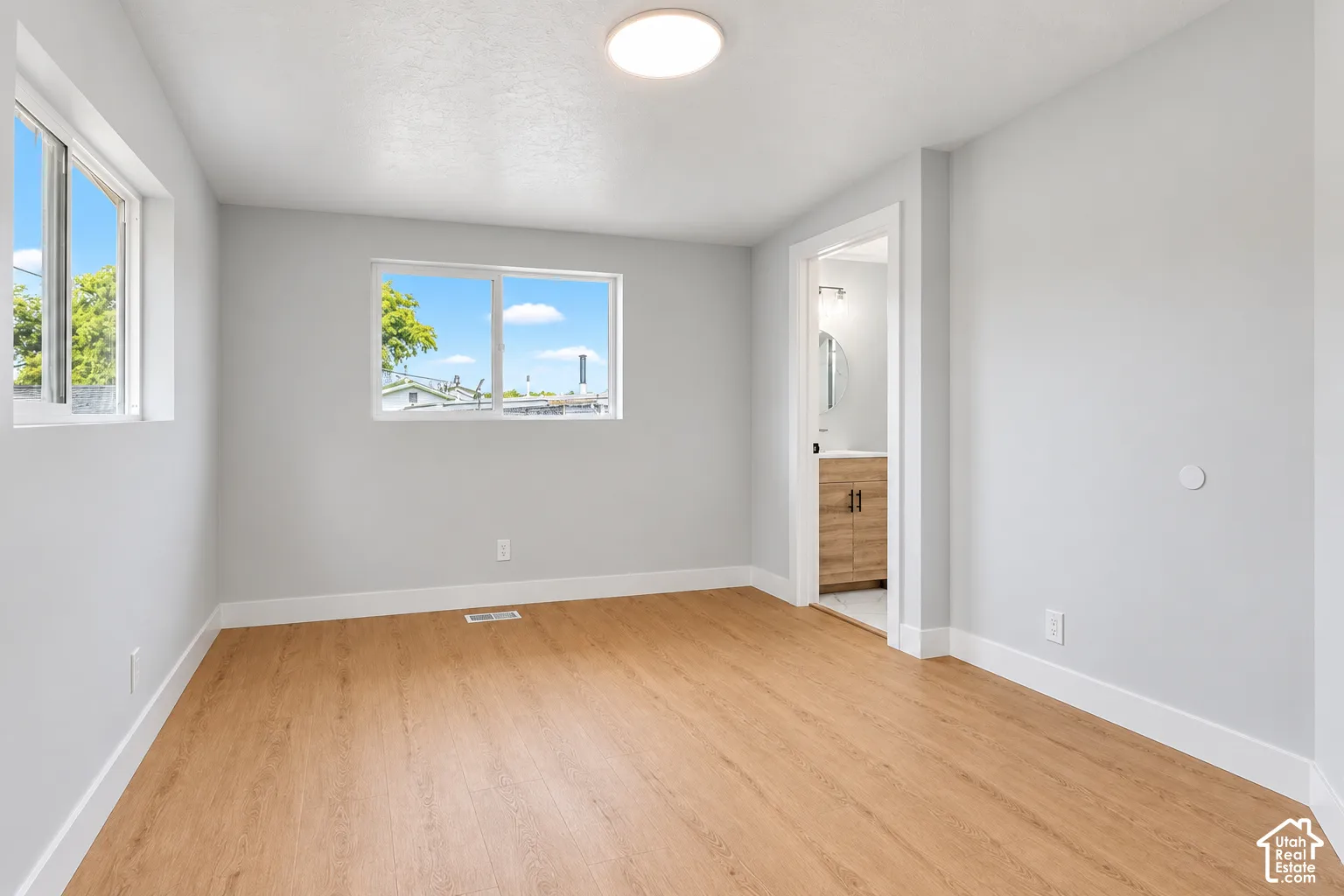 Neutral-toned interior featuring wood-finish flooring, dual sliding windows, and a flush-mount overhead light fixture