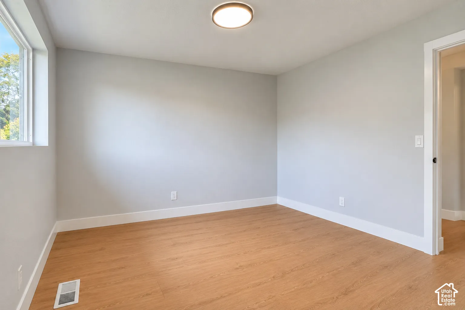 Neutral wall paint, wood-finish flooring, recessed ceiling lighting, and a window with white trim