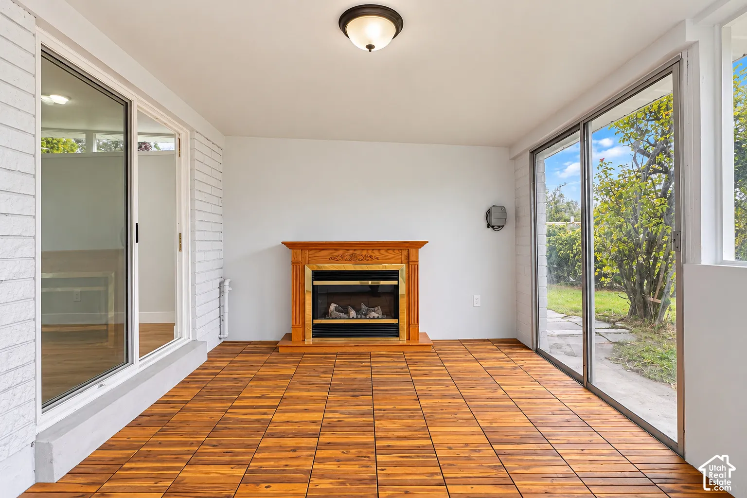 Enclosed sunroom featuring wood-finish flooring, white brick walls, a fireplace with a wood mantel, and sliding glass doors