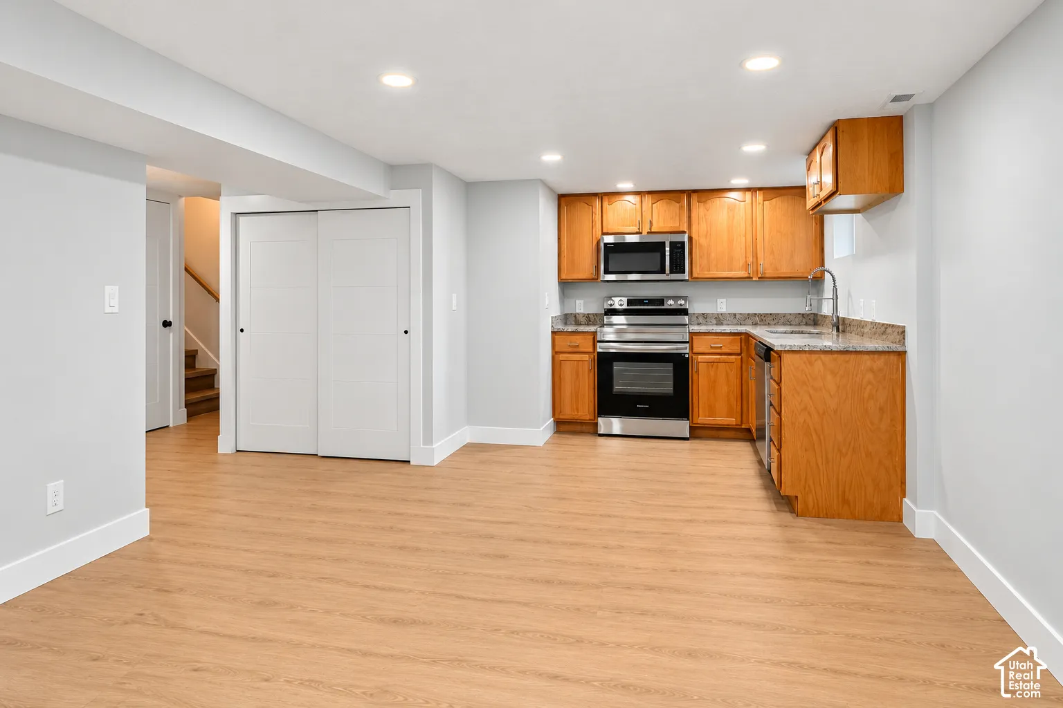 Kitchen area featuring wood cabinetry, stone-finish countertops, stainless steel appliances, wood-finish flooring, and recessed lighting