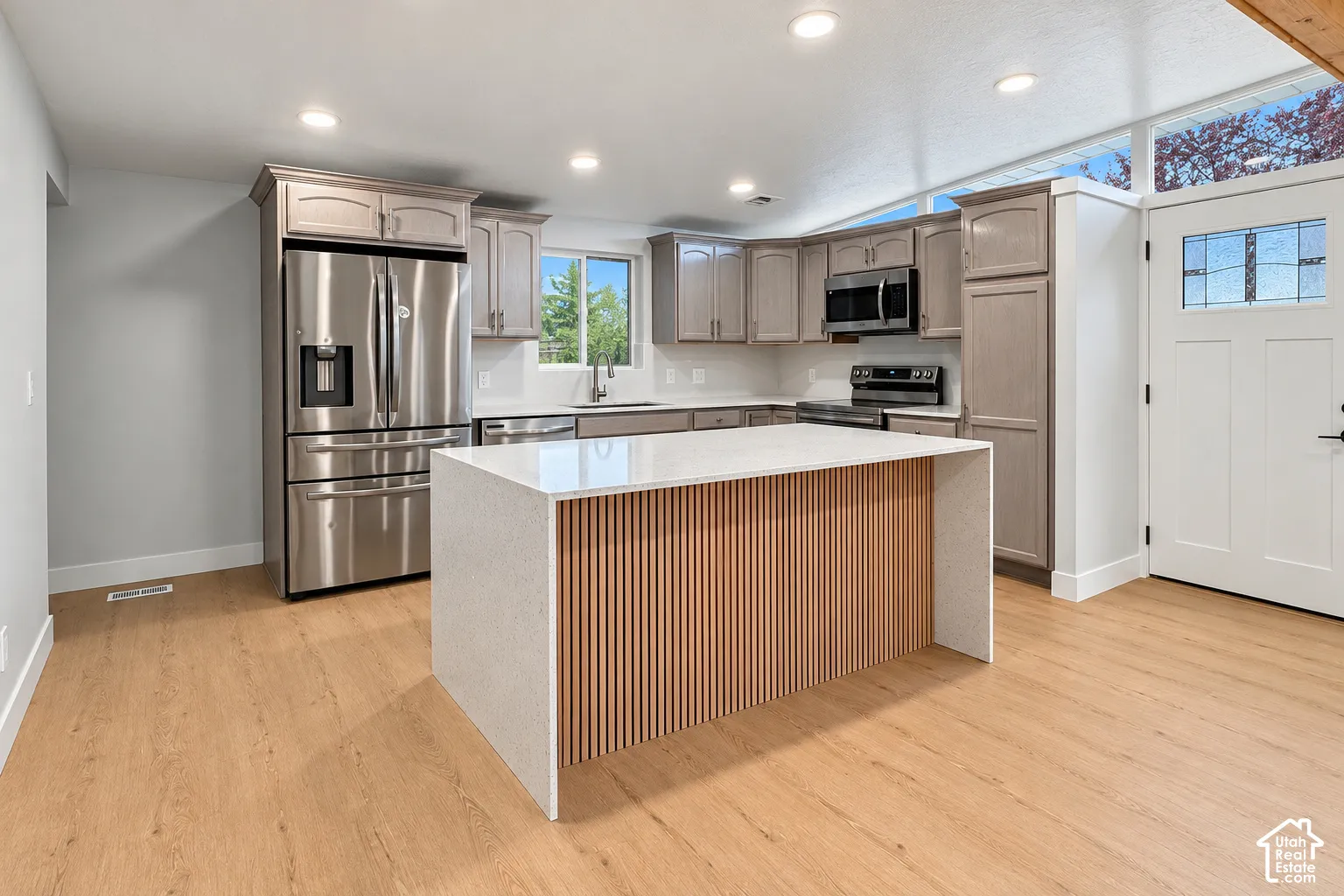 Kitchen featuring a central island with a waterfall countertop and vertical wood-slat detailing, stainless steel appliances, wood-finish flooring, and shaker-style cabinetry