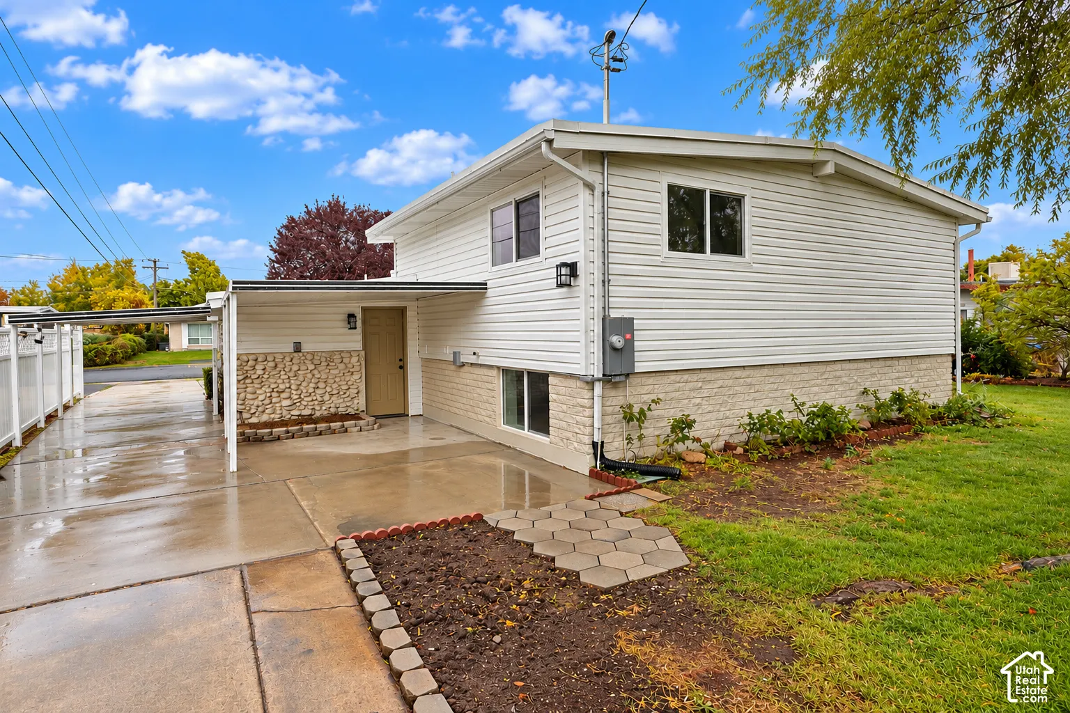 Exterior featuring white horizontal siding, textured stone masonry accents, a covered carport, and a paved concrete driveway