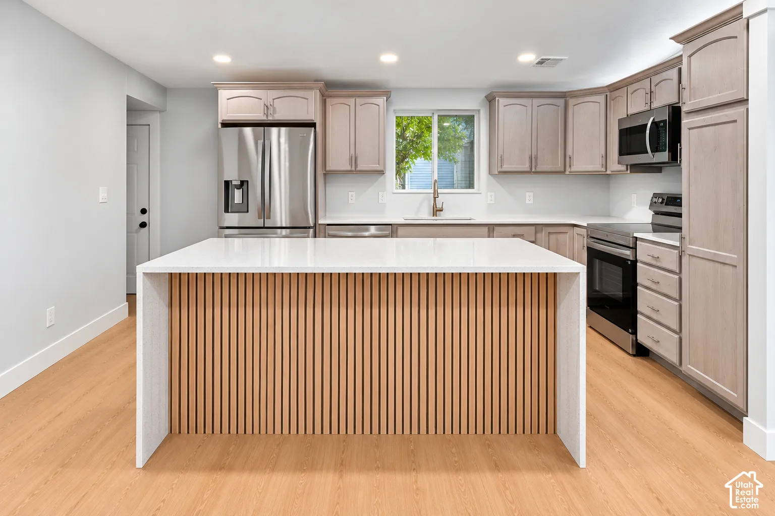 Kitchen featuring a waterfall island with a slatted wood-finish base, stainless steel appliances, light-toned cabinetry, and recessed lighting