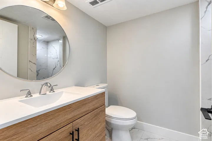 Wood-finish vanity cabinet, solid-surface countertop with integrated basin, circular mirror, and large-format tile flooring with marble-pattern veining