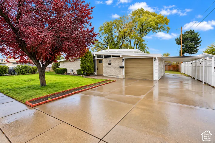 Mid-century modern exterior featuring stone masonry, a single-car garage, an attached metal carport, and a manicured lawn