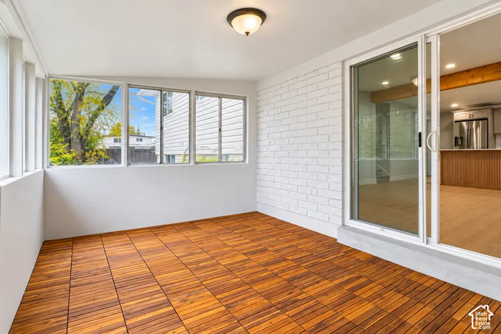 Enclosed sunroom featuring wood-finish flooring, white-painted brick wall, multi-pane window configuration, and sliding glass entry door