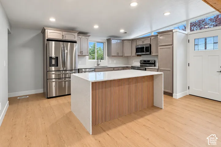 Kitchen featuring a central island with a waterfall-edge countertop and slat-wood detailing, stainless steel appliances, wood-finish flooring, and shaker-style cabinetry