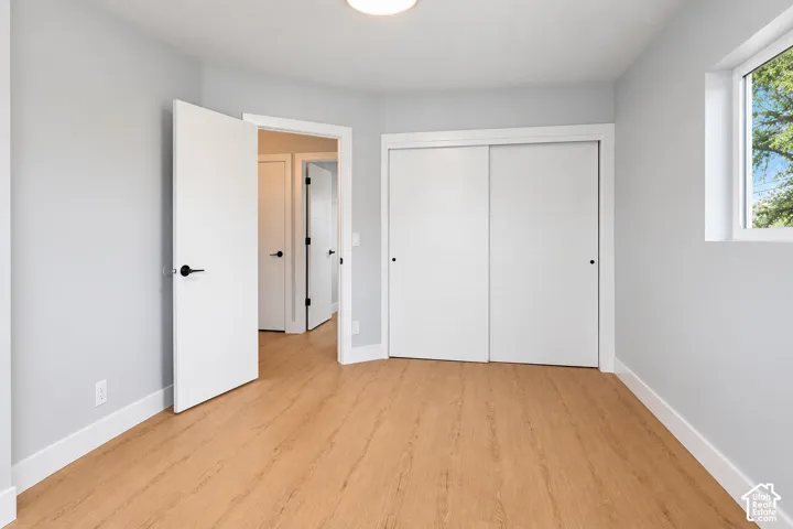 Room featuring wood-finish flooring, sliding closet doors, flush-mount lighting, and solid-core doors with matte black hardware