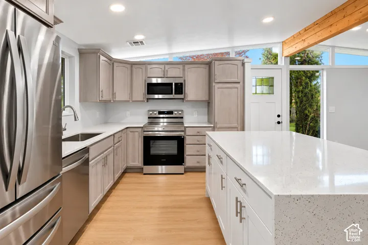 Kitchen featuring an expansive center island with stone-composite countertop, light wood-tone cabinetry, stainless steel appliances, recessed ceiling lighting, and clerestory windows