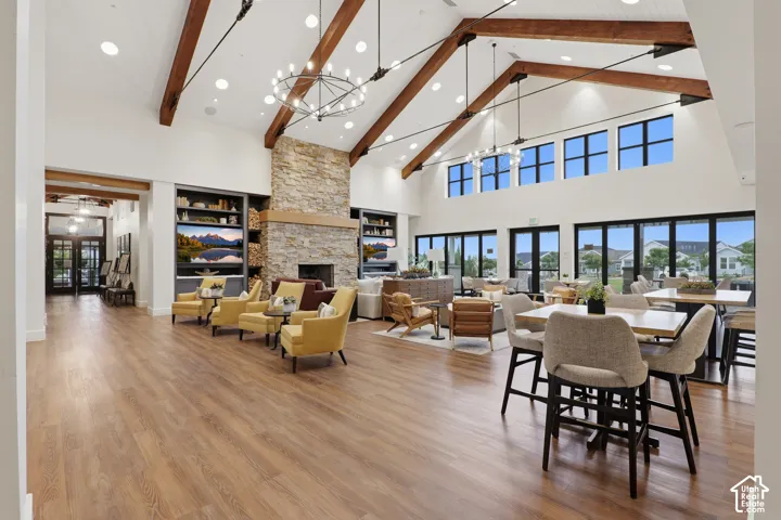 Vaulted ceiling with exposed wood beams, full-height stone fireplace, wood-finish flooring, custom built-in cabinetry, and multi-panel glass doors