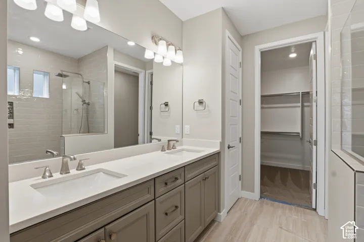 Dual-sink vanity with neutral-tone cabinetry and quartz countertops, full-width wall mirror, walk-in shower with tile surround, and tile flooring