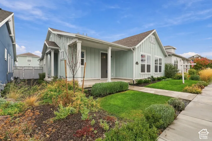 Board-and-batten siding exterior featuring a covered front porch with square columns, a concrete walkway, and landscaped garden beds