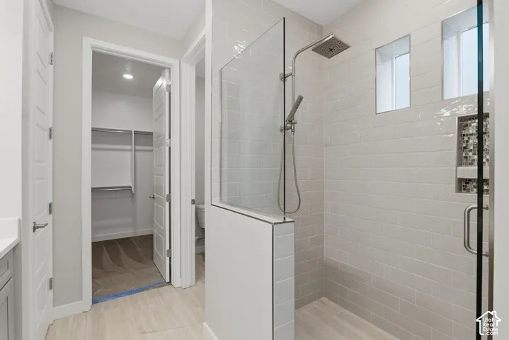 Walk-in shower featuring subway tile surround, glass panel enclosure, rainfall showerhead with handheld attachment, and an integrated tiled niche with mosaic accent