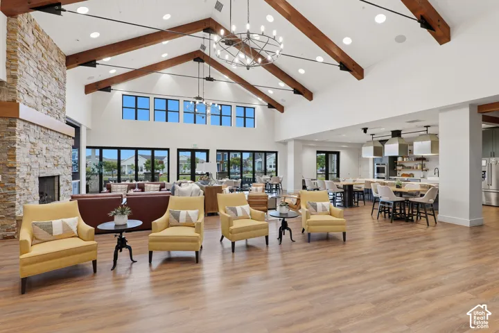 Vaulted ceiling featuring exposed wood beams, stone-clad floor-to-ceiling fireplace, expansive multi-panel glass doors, wood-finish flooring, and industrial-style tiered chandeliers