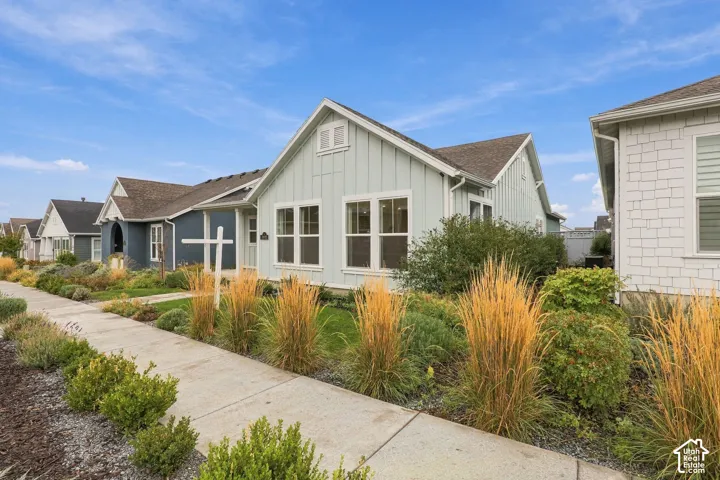 Light green board-and-batten siding, gable roofline, multi-pane windows, and landscaped front yard with ornamental grasses