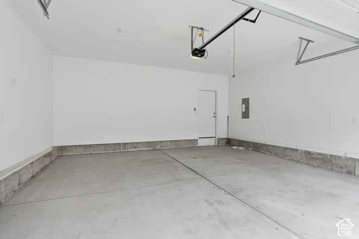 Garage featuring finished white walls, concrete flooring, an integrated automated door opener, and a single pedestrian entry door