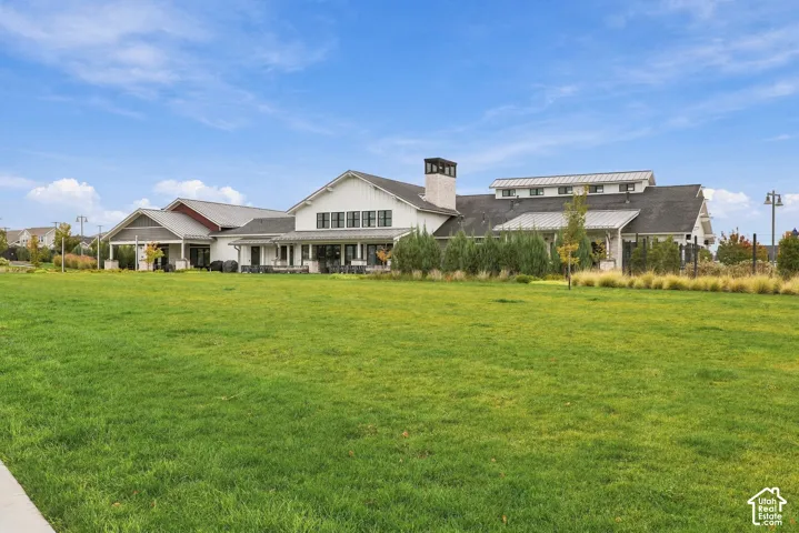 Expansive landscaped grounds featuring mature trees and shrubs, highlighted by a multi-section structure with a metal roof, white siding, stone chimney, and multi-paned windows