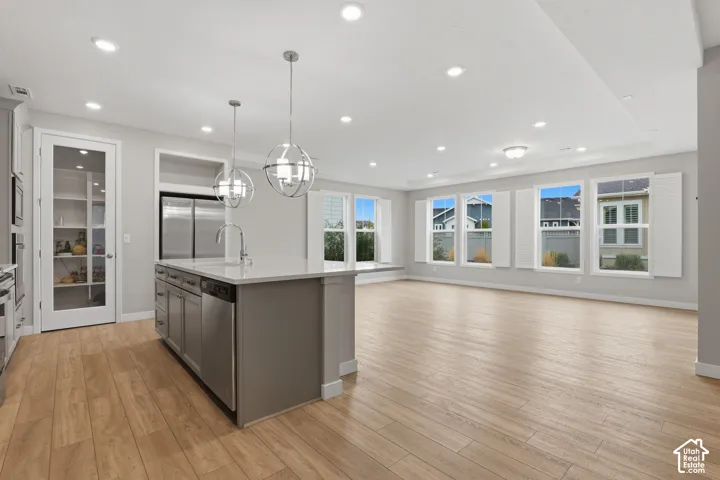 Kitchen featuring an expansive island with stone-style countertops, wood-finish flooring, recessed lighting, spherical pendant fixtures, and a walk-in pantry with a glass-paneled door