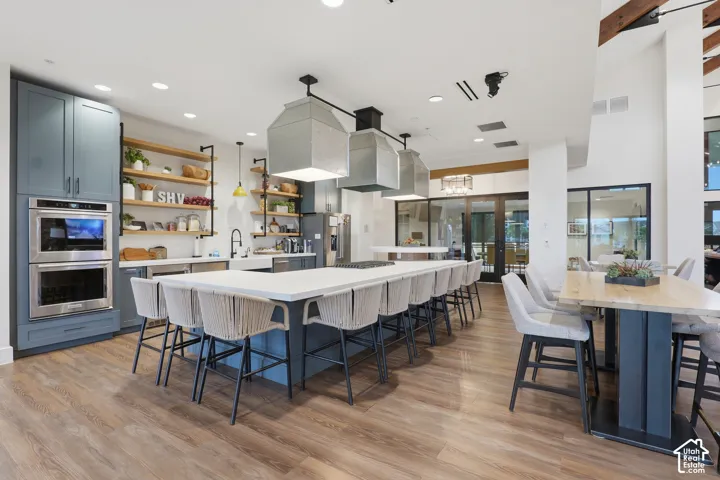 Kitchen featuring blue cabinetry, quartz countertops, dual metal-cased pendant lighting, wood-finish flooring, and floating wood shelving
