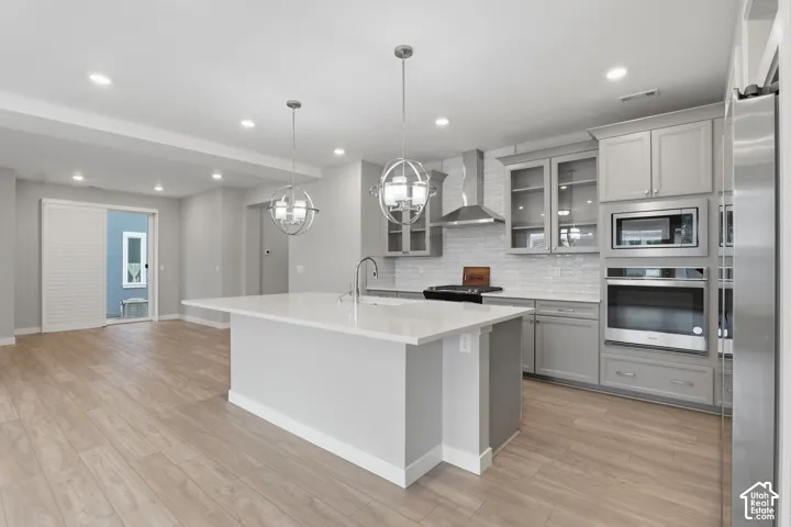 Kitchen featuring an oversized quartz-topped island, light gray shaker-style cabinetry, stainless steel built-in double wall ovens, glass-front upper cabinet displays, and wood-finish flooring